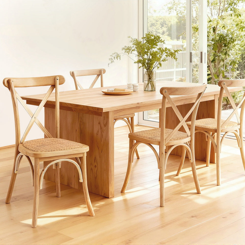 Wooden dining table with four matching chairs in a bright room with large windows.