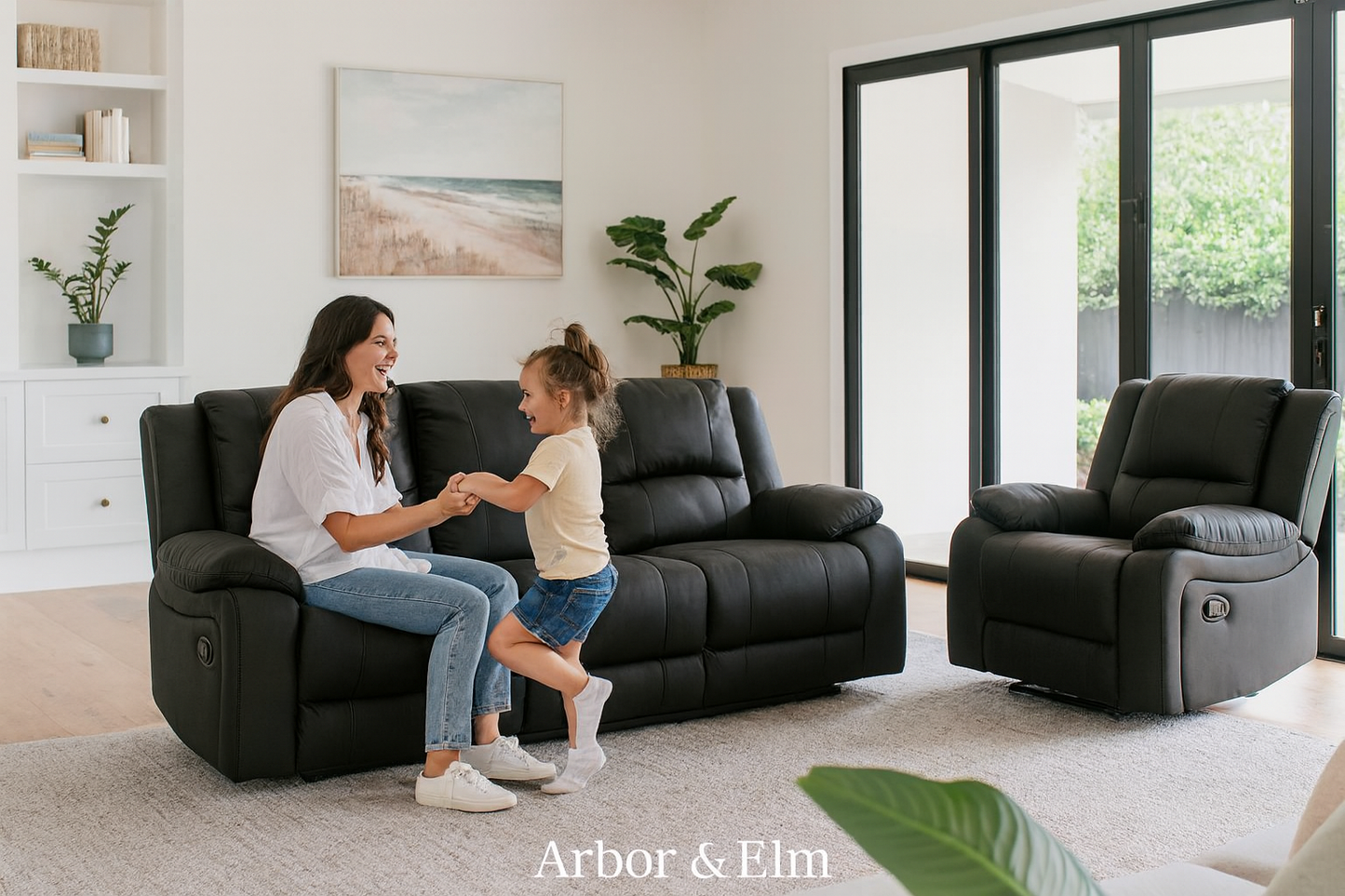 Woman and child interacting in a living room with black recliner chairs, Arbor & Elm branding visible.
