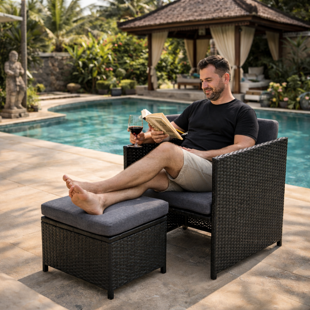Man relaxing on outdoor furniture by a pool, reading a book and drinking wine.